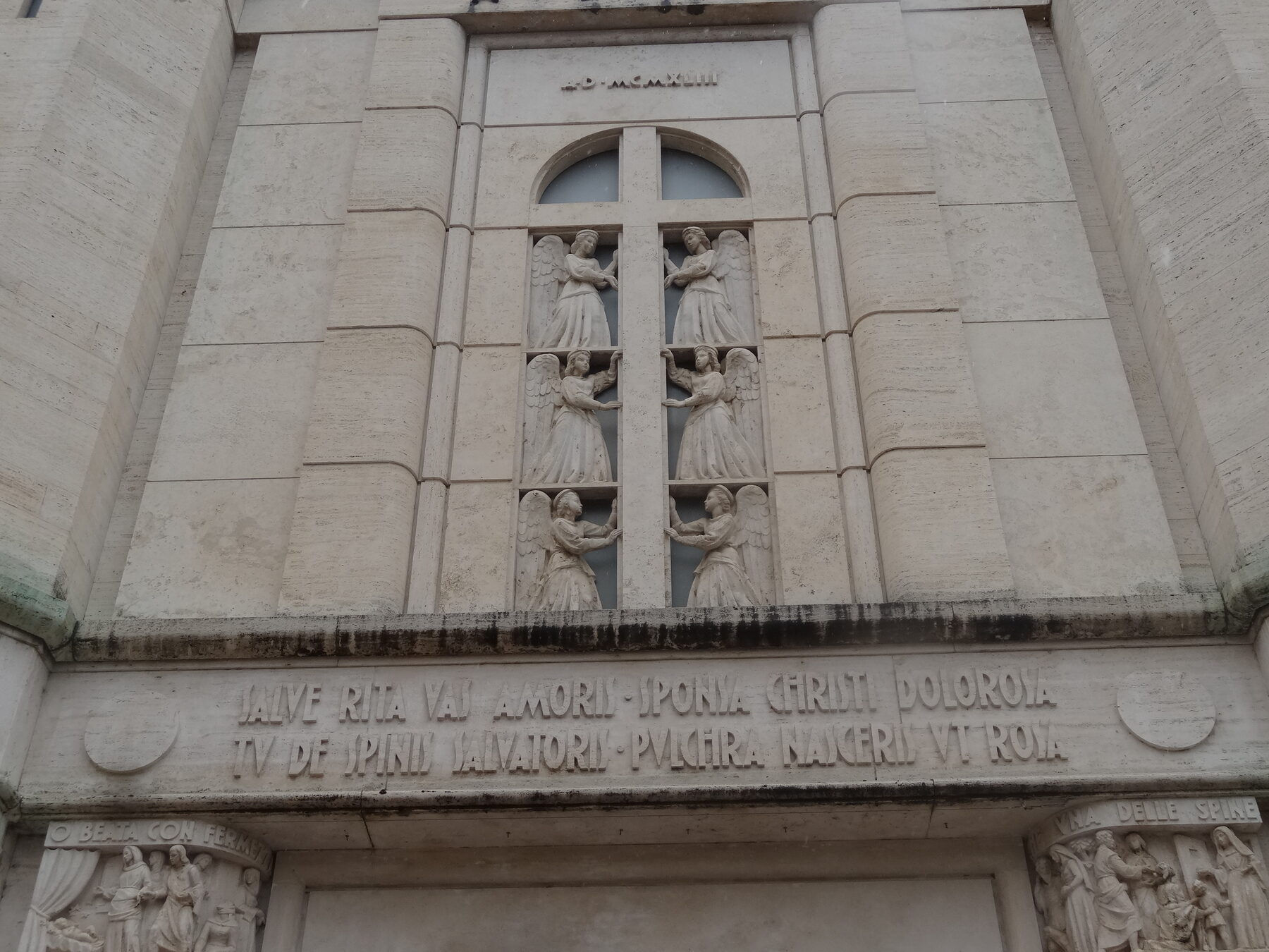 Detalle de la fachada de la basílica de Santa Rita de Cascia, con relieves de ángeles y una inscripción en latín