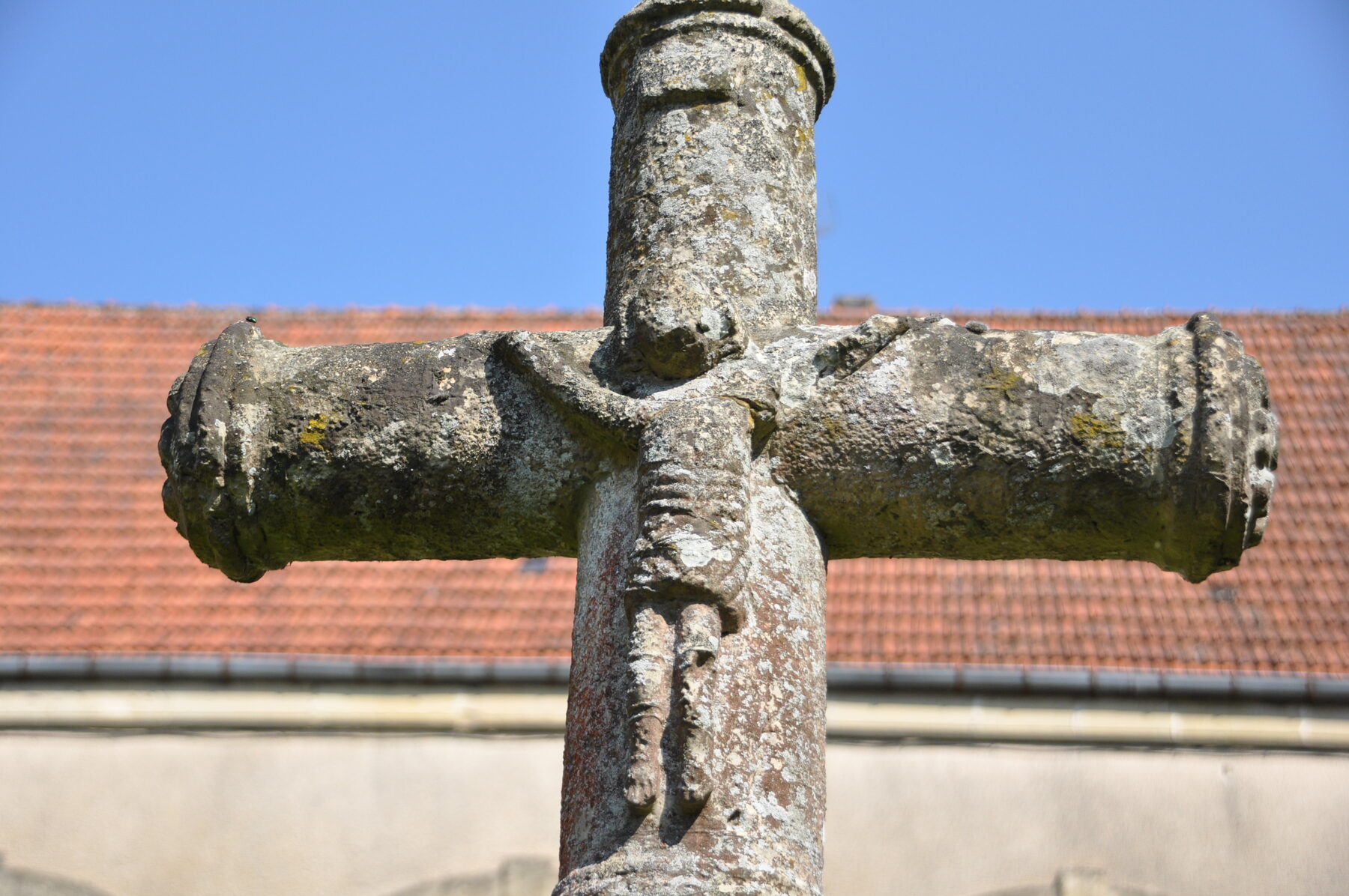 Cruz de piedra con un Cristo tallado, junto a tejados rojos, en Faverney