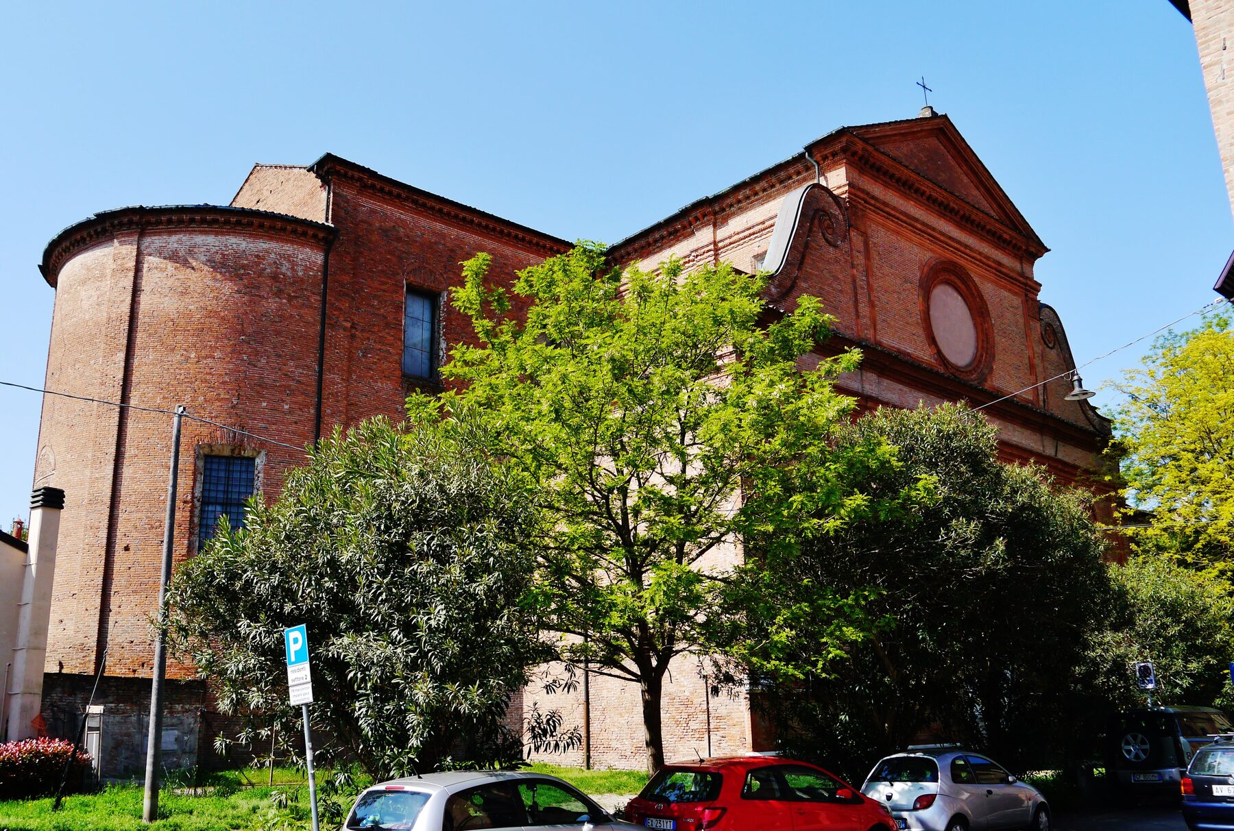 Exterior de ladrillo de la basílica de Santa Maria in Vado de Ferrara, con su ábside redondeado y árboles delante