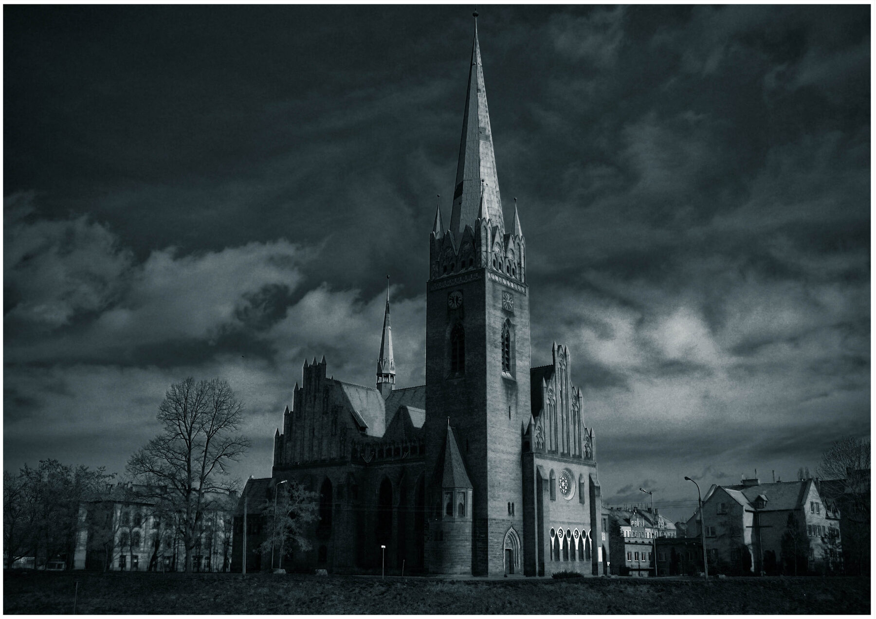 La iglesia de San Jacinto de Legnica con su alta torre gótica, en una fotografía en blanco y negro con nubes oscuras
