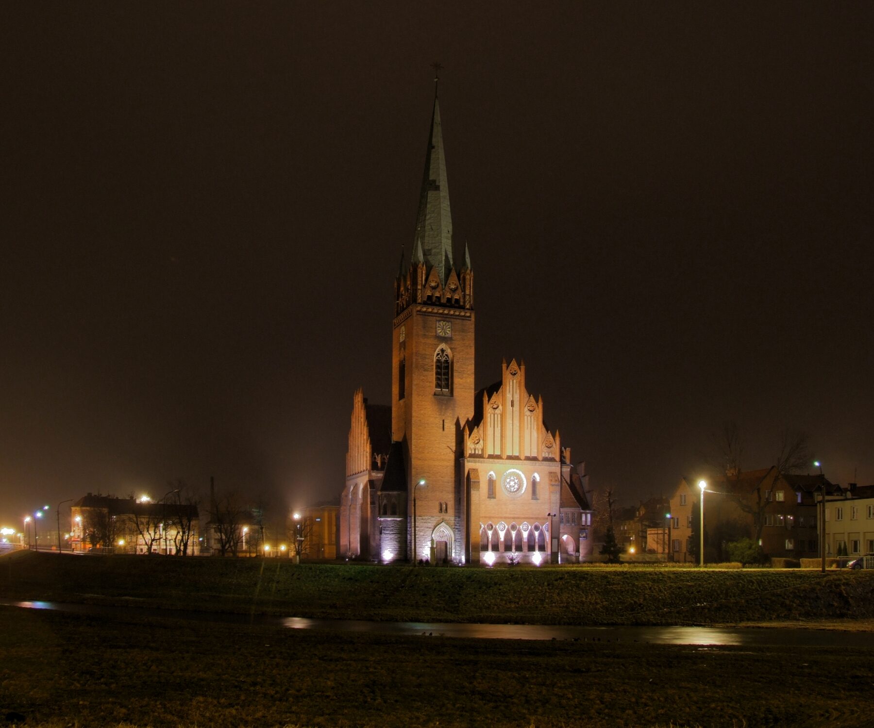 La iglesia de San Jacinto de Legnica iluminada de noche, con su torre y sus muros de ladrillo
