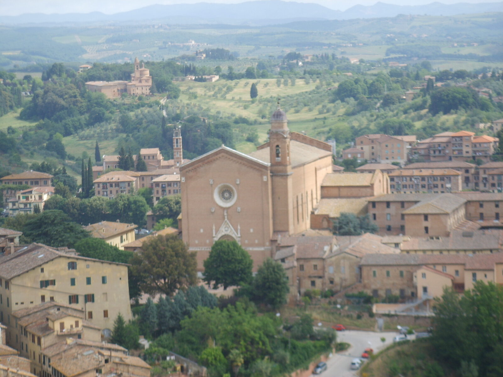 Vista de la basílica de San Francisco de Siena desde lo alto, entre casas y colinas de la Toscana