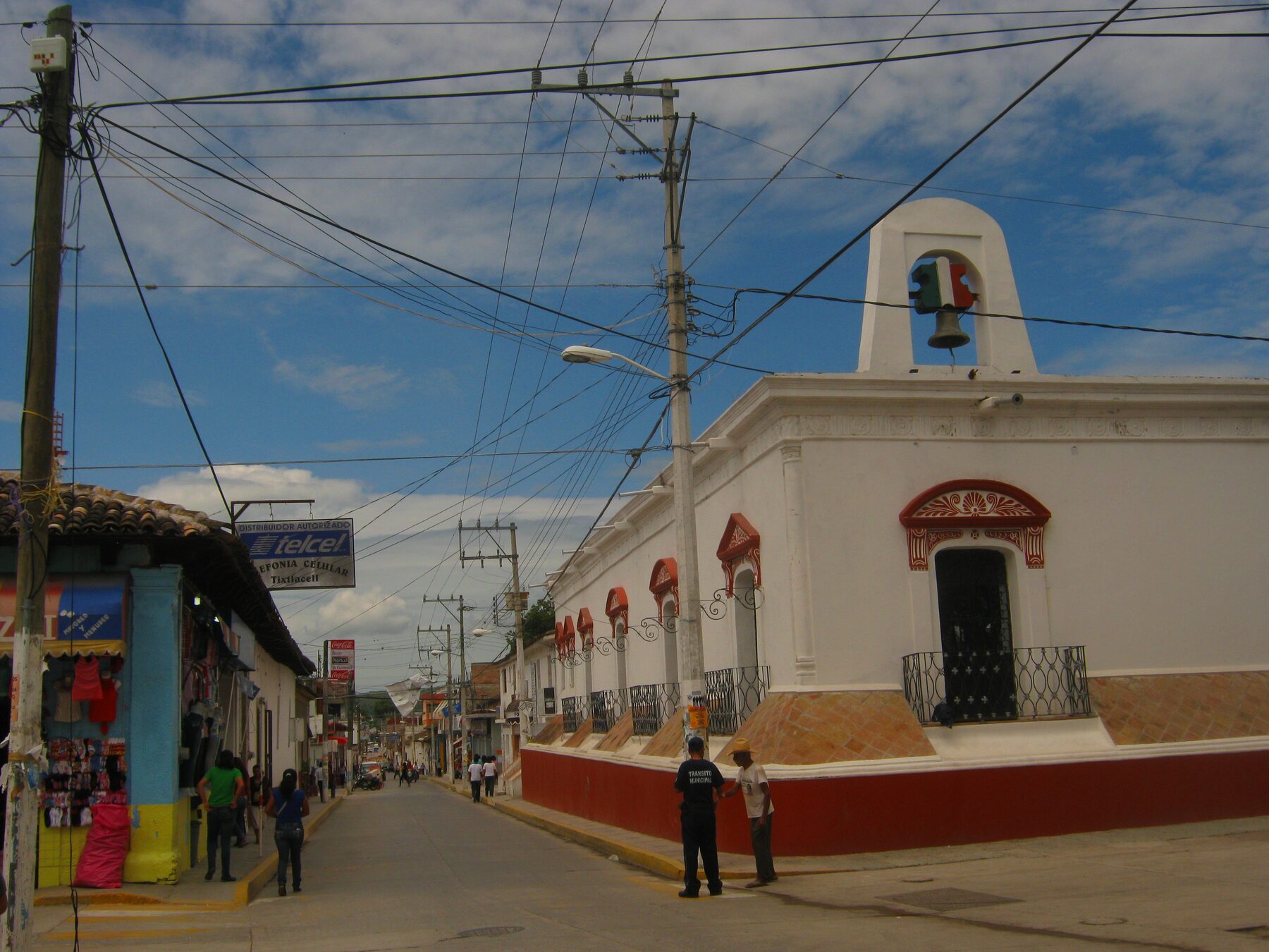 Calle de Tixtla de Guerrero con edificios blancos y rojos y un campanario, bajo un cielo con nubes